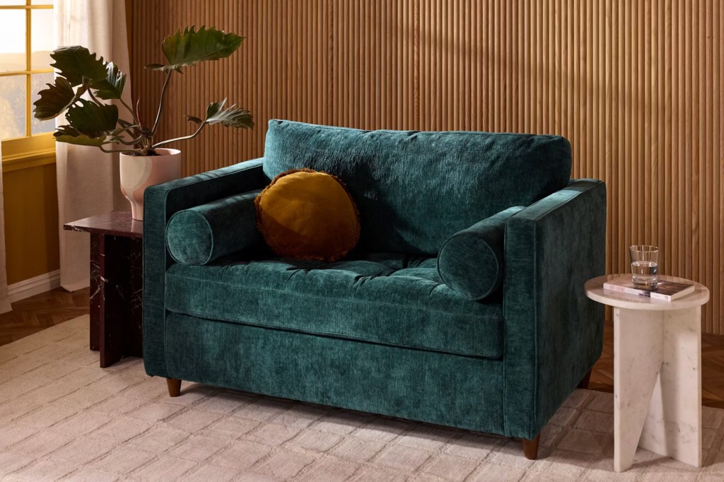 Green velvet sofa bed with round pillows in a modern living room with wood panel walls