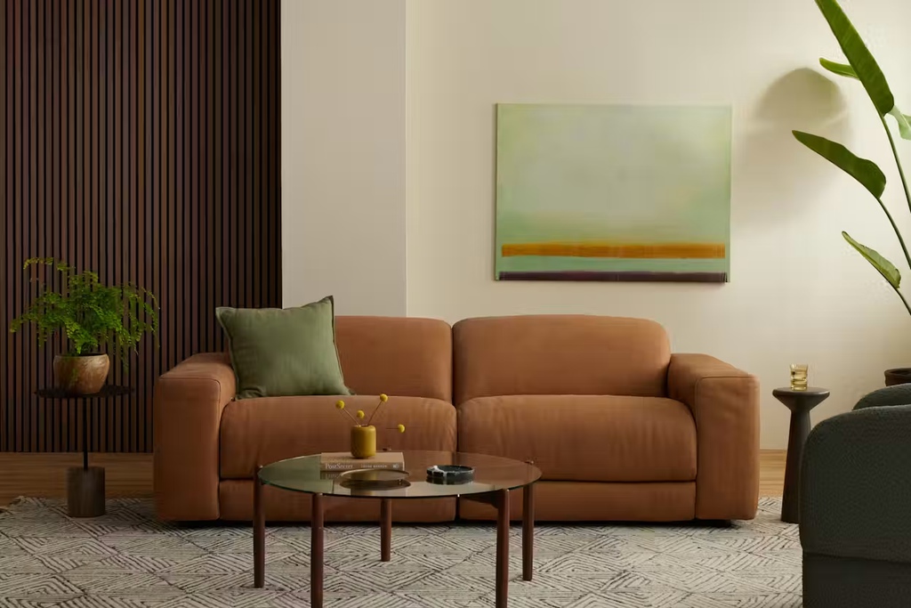 Brown leather reclining sofa in a modern living room with a round glass coffee table and warm wood accents