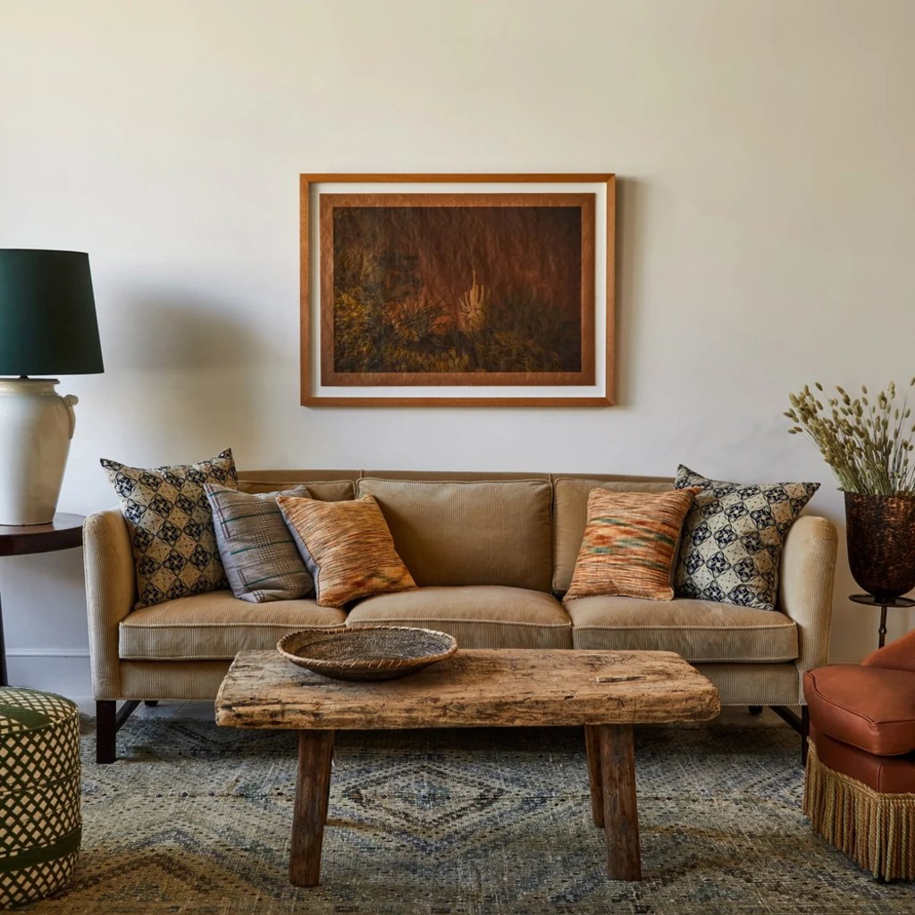 Tan high-arm sofa with patterned throw pillows and a rustic wood coffee table in a warm eclectic living room.
