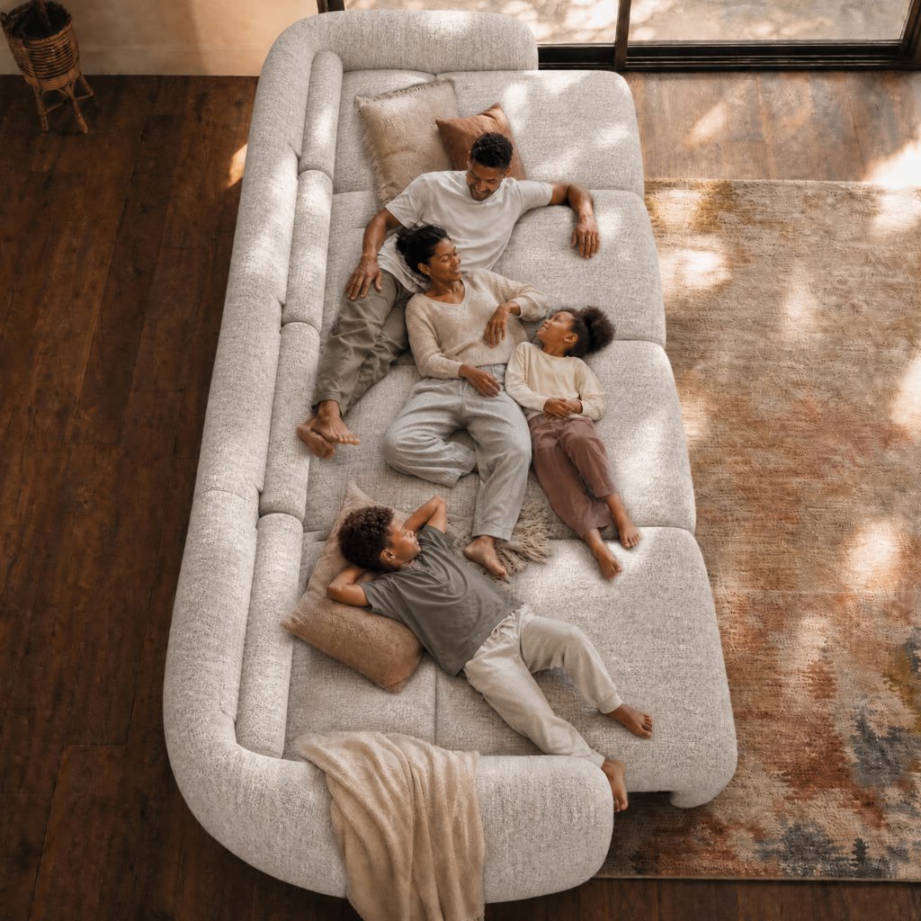 Family relaxing together on a large cream sofa bed in a warm living room.