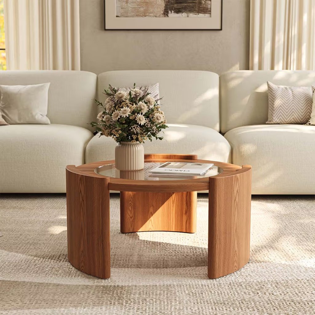 Large round wood and glass coffee table with curved legs in front of a cream sofa in a bright living room.