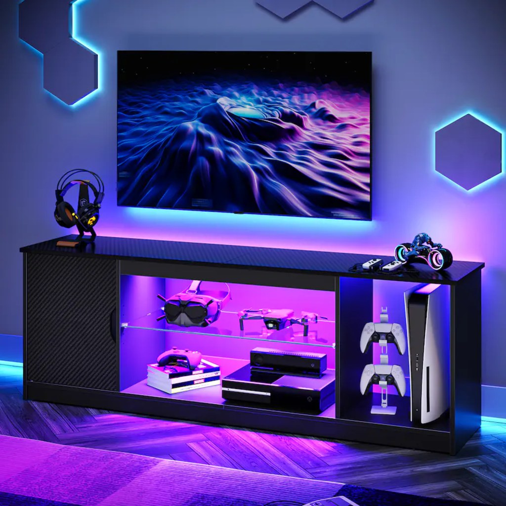 PS5 console and controllers displayed in an LED-lit gaming TV stand beneath a wall-mounted TV.
