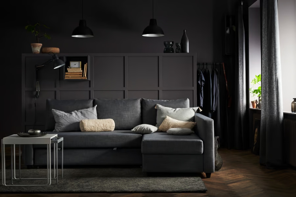 Dark gray sectional sofa bed with cushions in a modern living room with black walls and wood flooring
