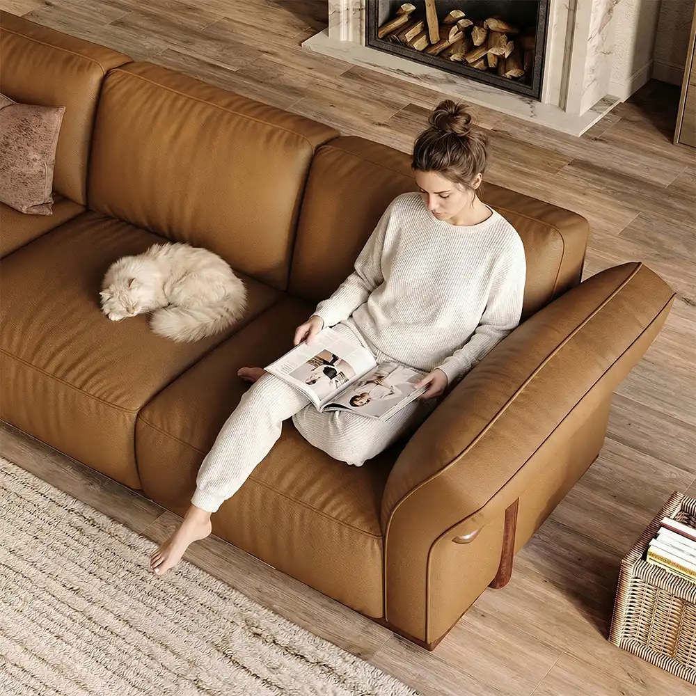 Woman reading on a brown leather sofa beside a sleeping cat in a warm living room.