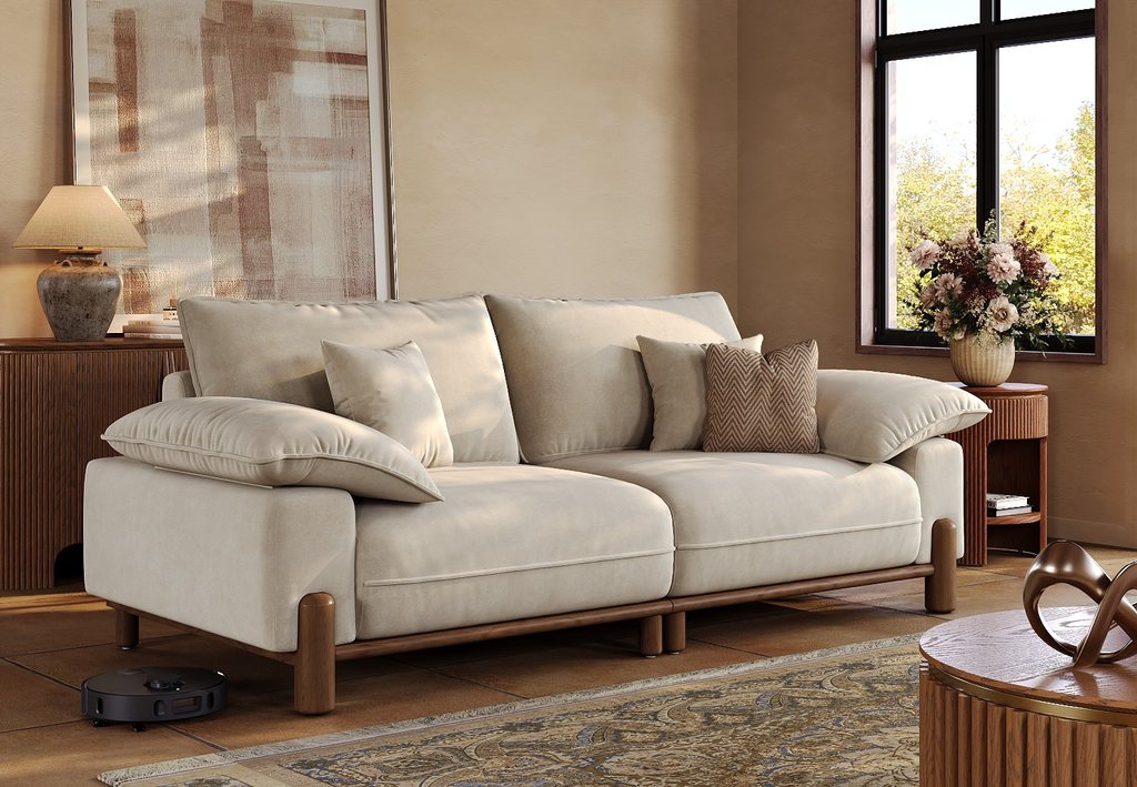 Cream low-arm sofa with oversized cushions and a wood base in a warm modern living room.