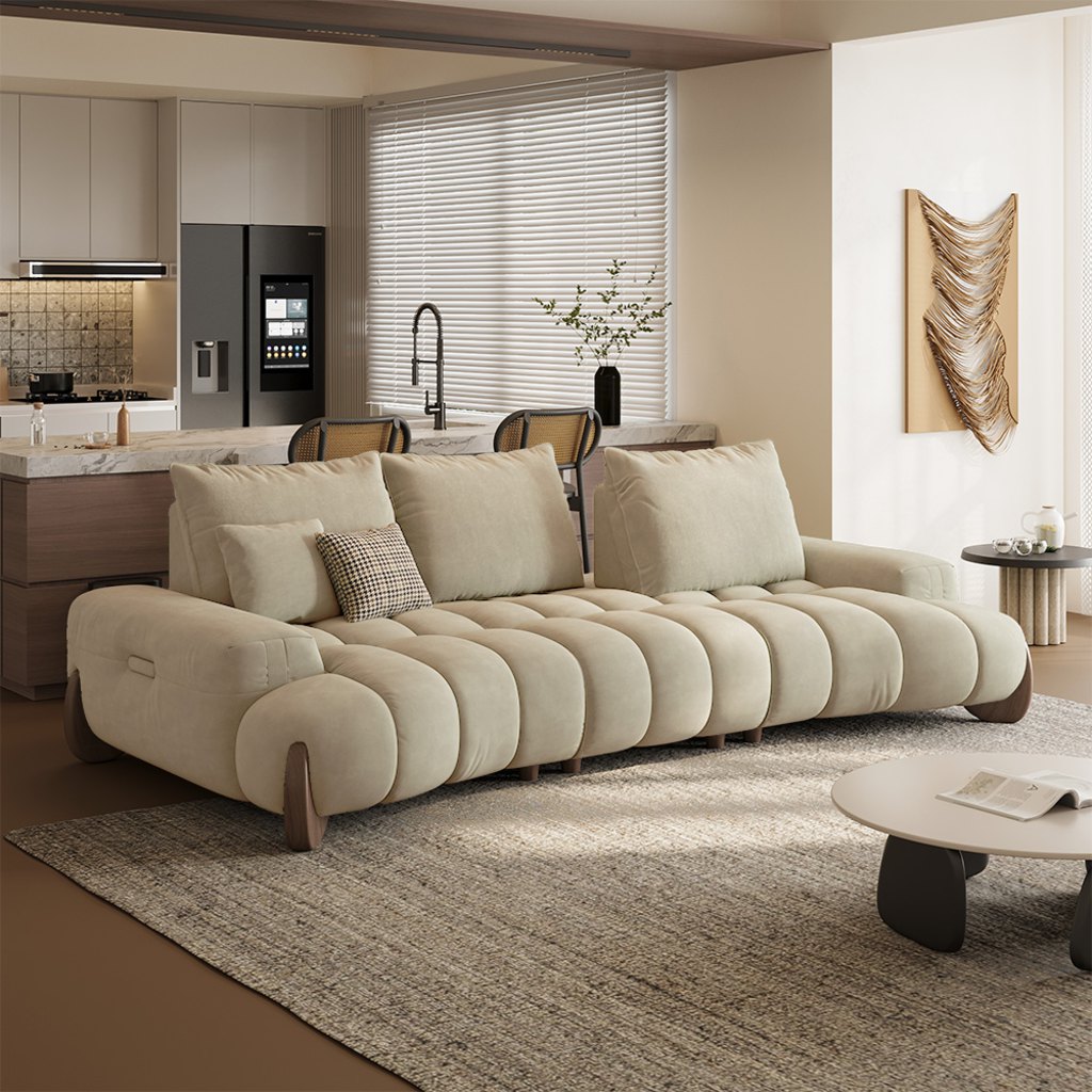 Cream low-arm sofa with rounded channel-tufted cushions in a modern open-plan living room and kitchen.