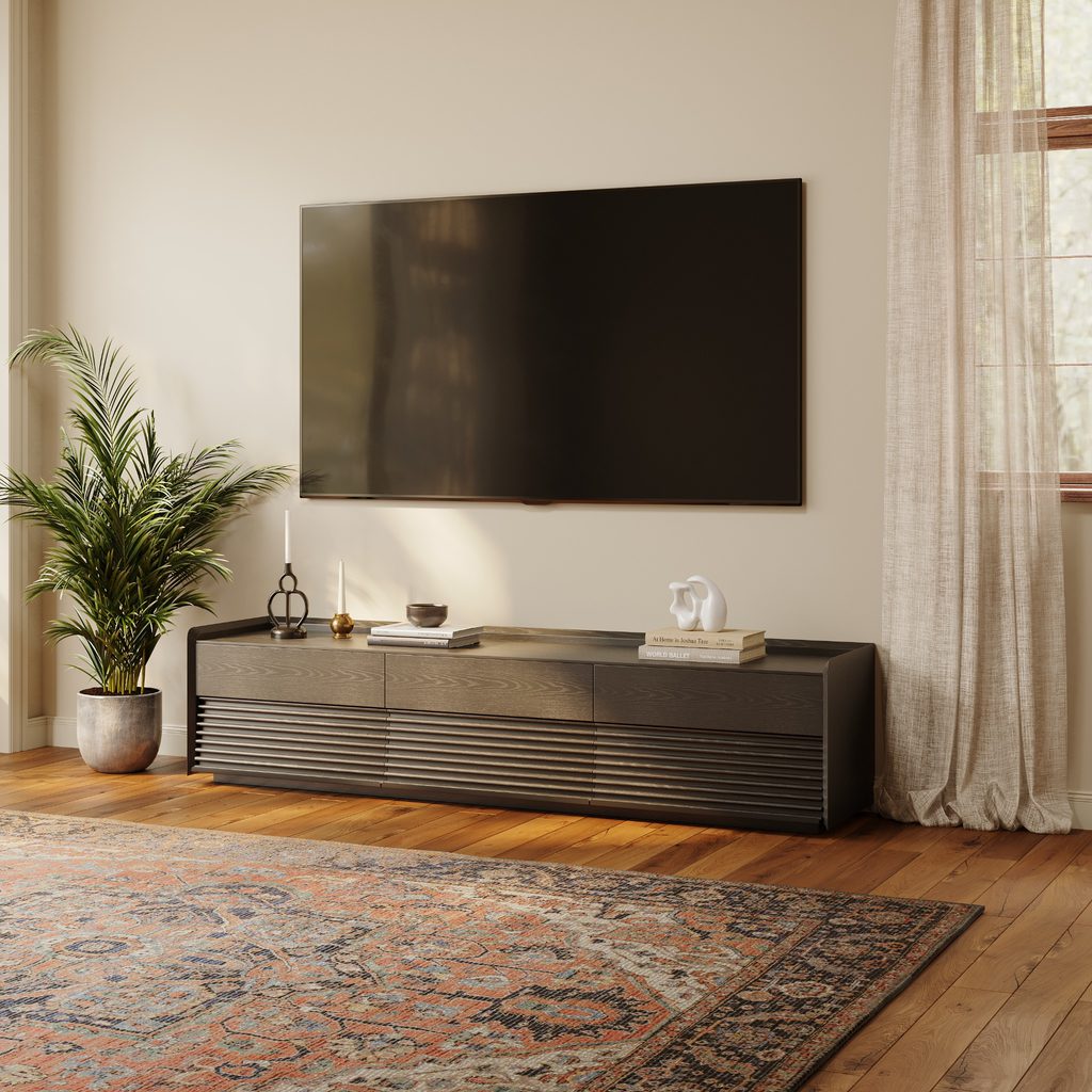 Modern Victorian living room with a dark wood media console, wall-mounted TV, patterned rug, warm wood floors, and sheer curtains.
