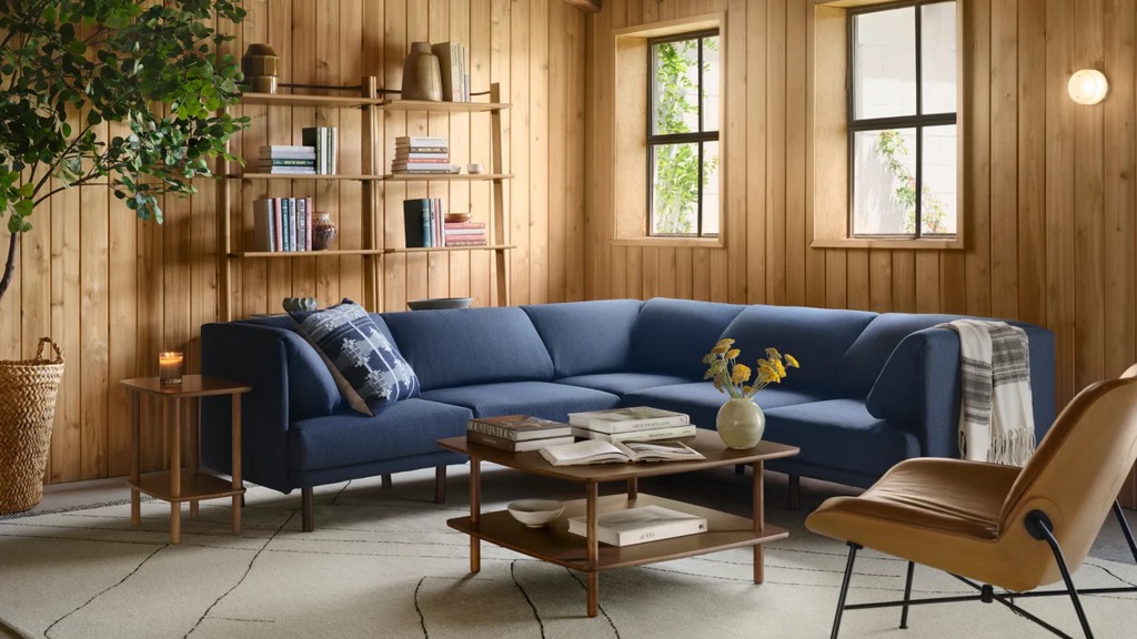 Blue sectional sofa with books and an open book on the coffee table in a warm wood-paneled reading room.