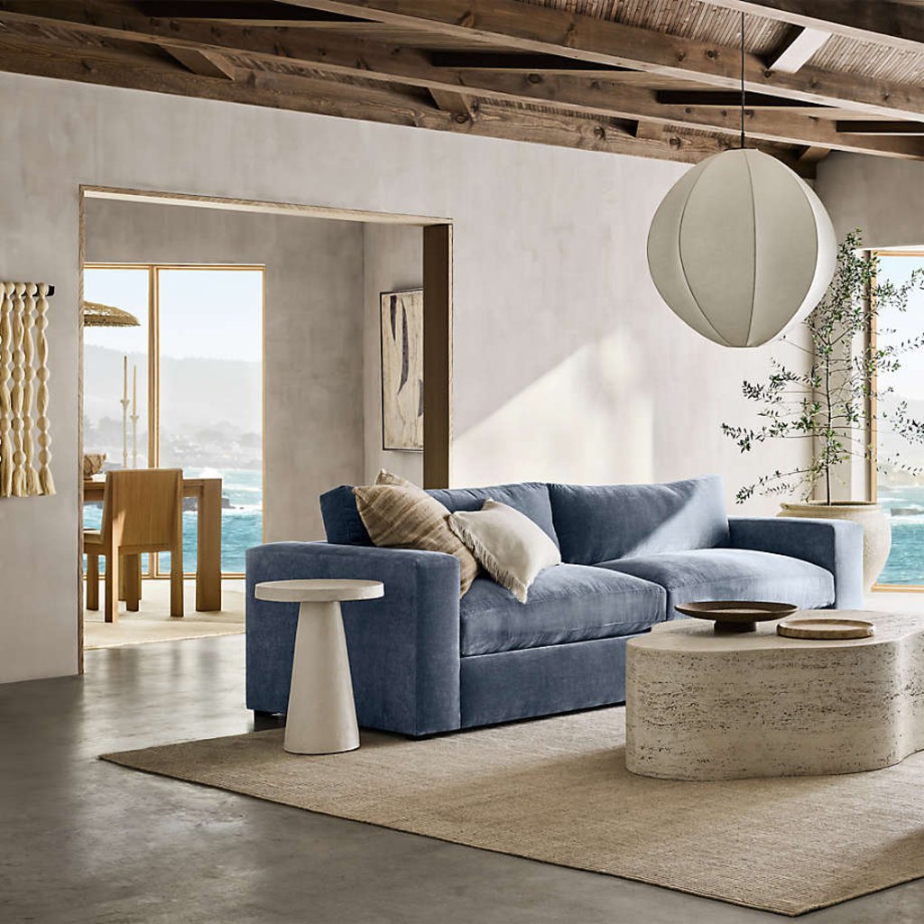 Blue low-arm sofa with deep cushions in a coastal modern living room with exposed wood beams and ocean views.
