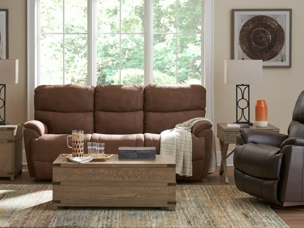 Brown three-seat reclining sofa in a bright living room with a large window and wooden coffee table