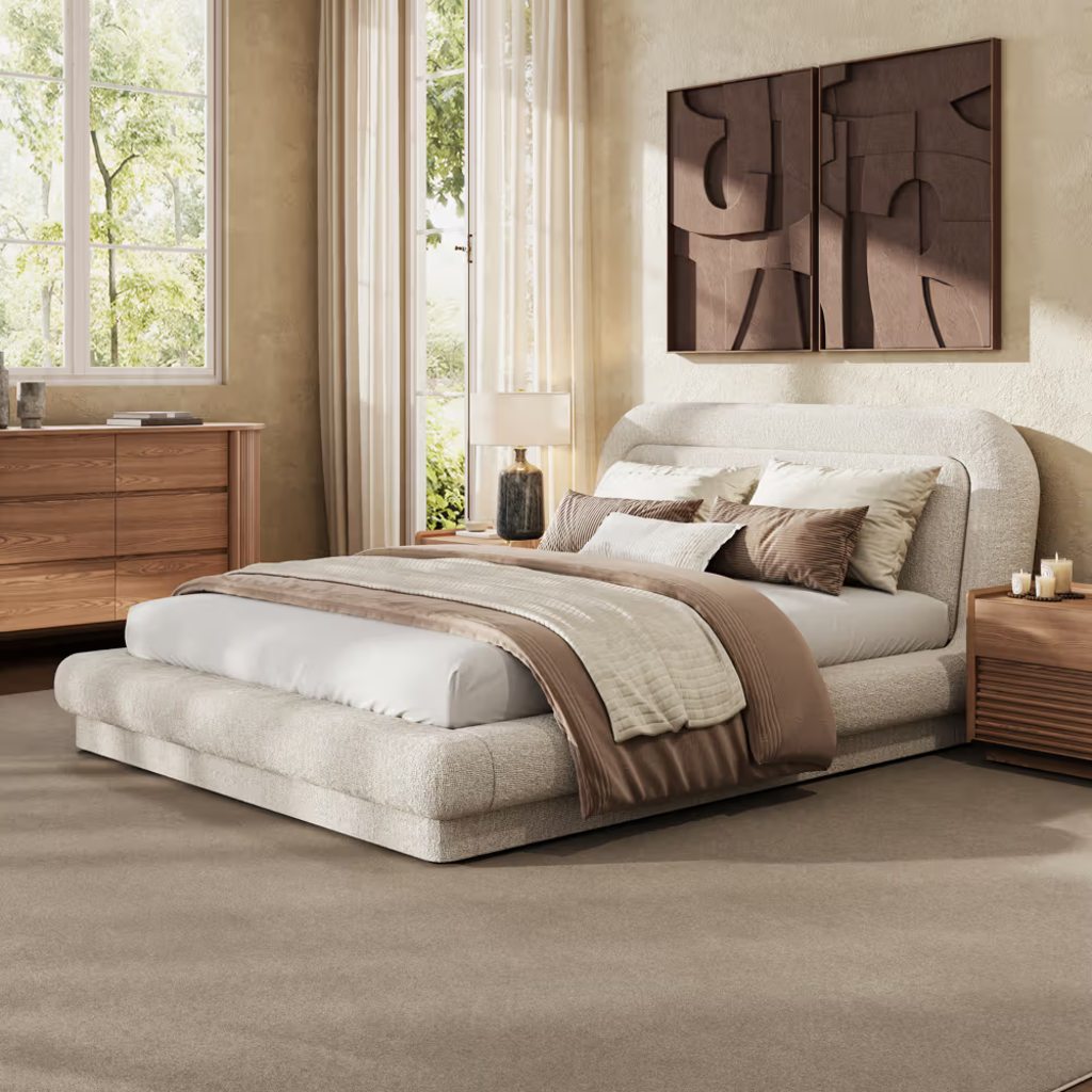 Beige upholstered bed with layered neutral bedding in a bright modern bedroom.