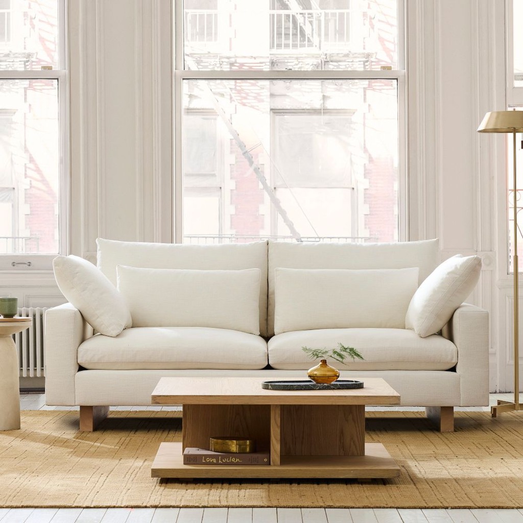 White upholstered sofa with layered cushions beside a floor lamp in a bright living room.