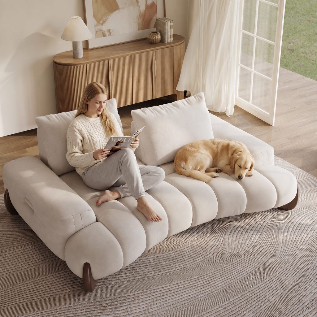 Oversized extra-deep beige sofa with wide cushioned seats, a woman reading, and a dog resting beside her in a bright living room