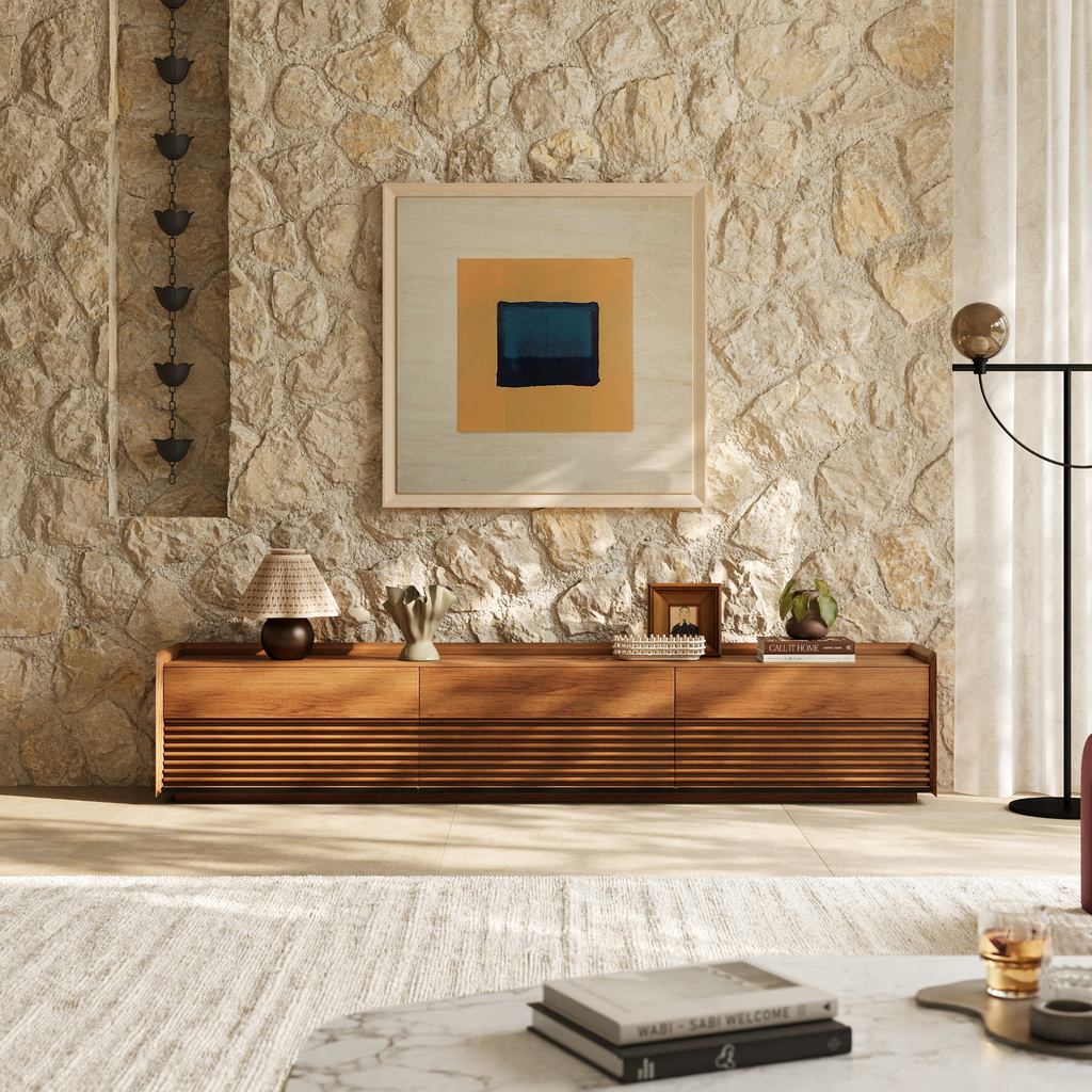 Modern Mediterranean living room with a warm walnut media console, textured stone wall, neutral rug, contemporary artwork, and soft natural light.