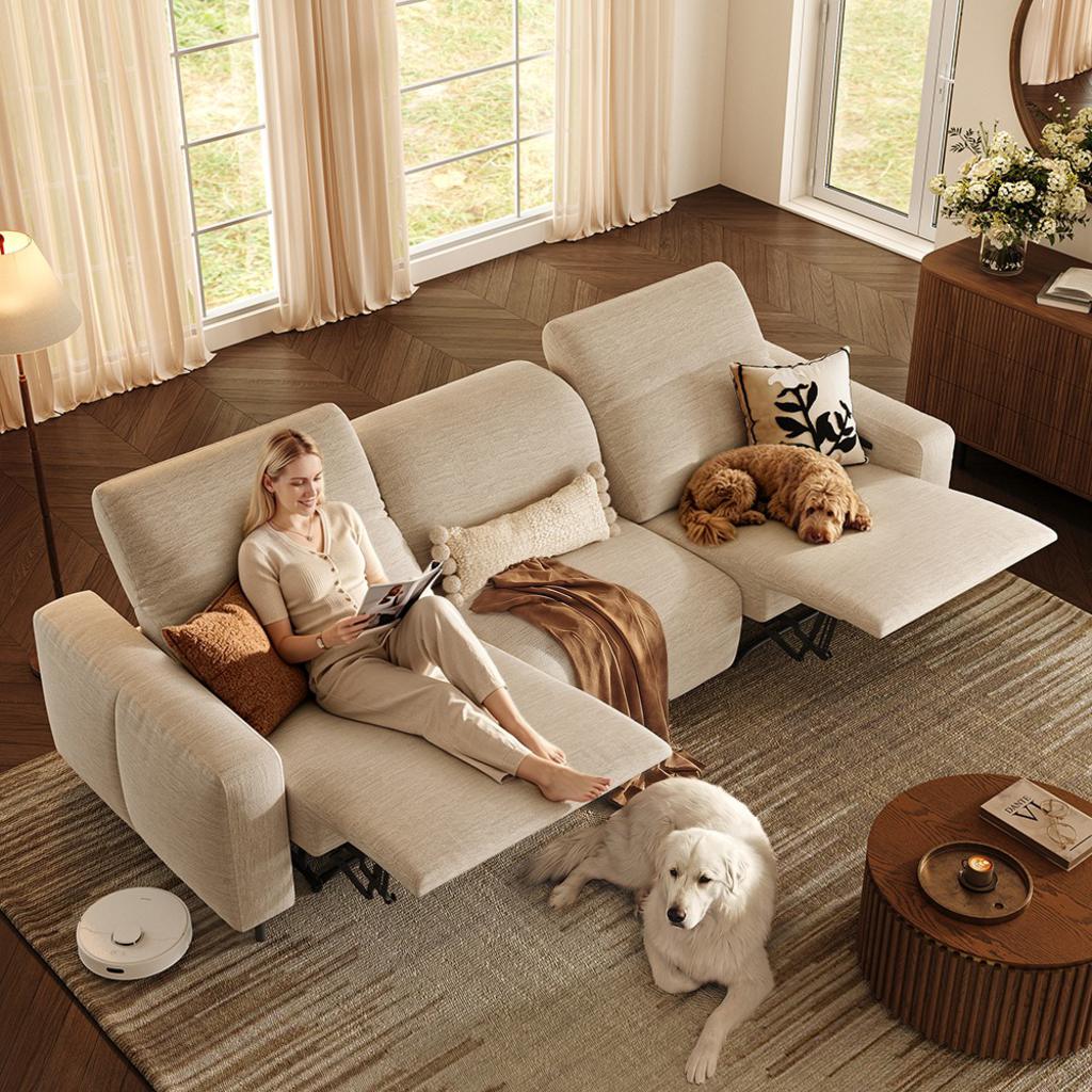Woman reading on a beige power reclining sectional sofa with adjustable headrests and two dogs in a bright living room.