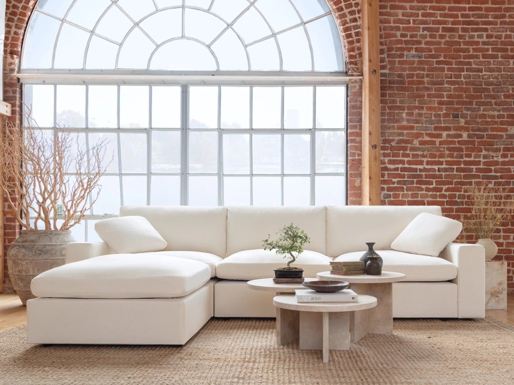 White chaise sectional sofa with loose cushions in a bright loft living room with exposed brick walls and large arched windows.