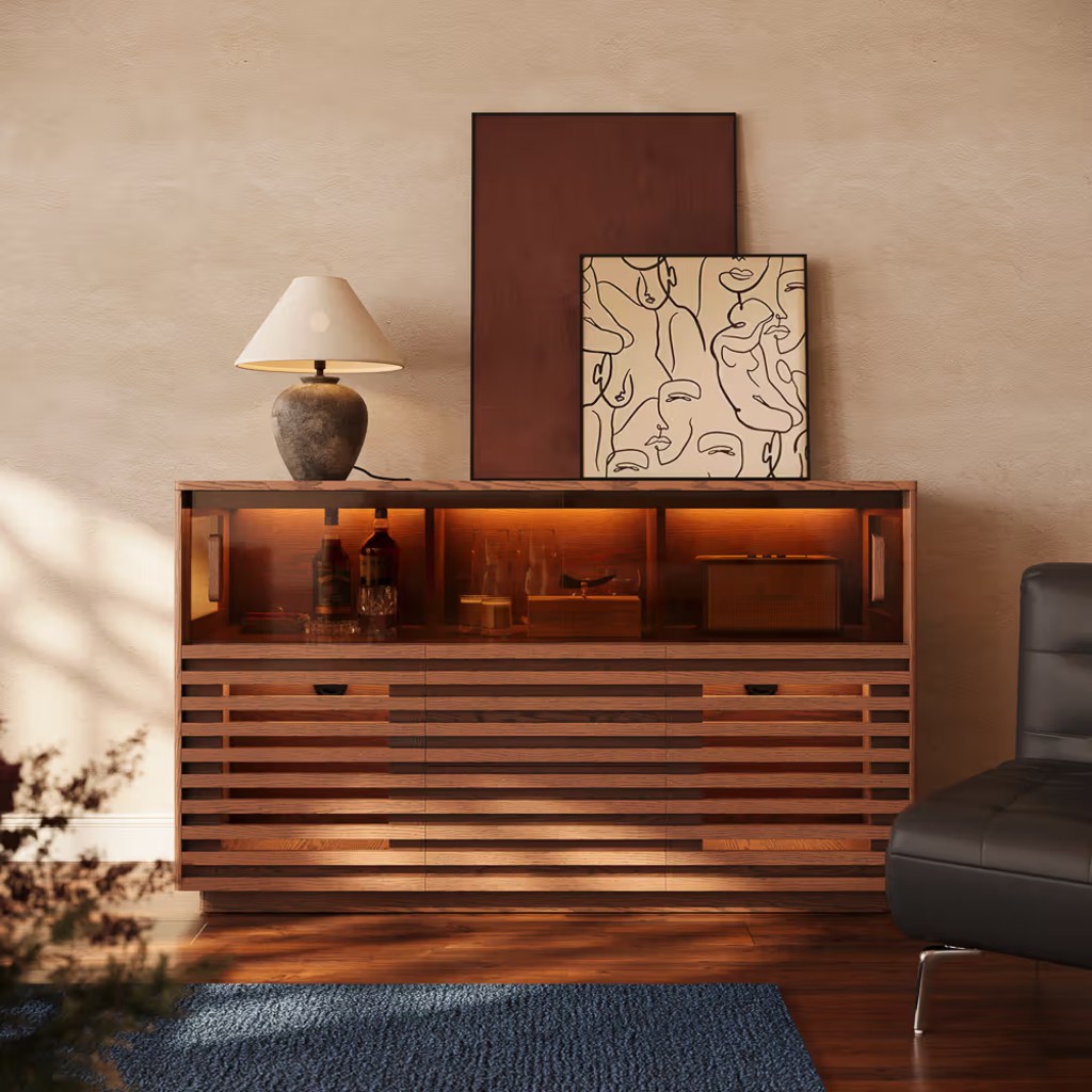 Warm wood storage cabinet with slatted drawers, illuminated open shelves, table lamp, and framed artwork.