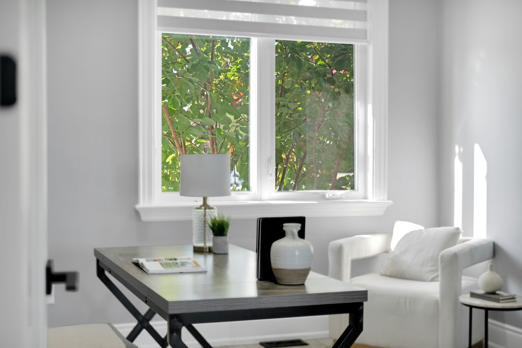 Bright living room office with a desk and white armchair beside a large window.