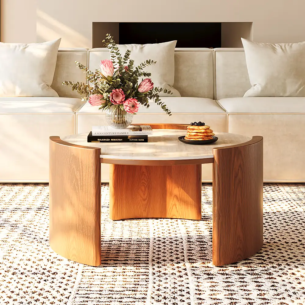 Round wood coffee table with a light stone top in front of a cream sofa, styled with flowers, books, and warm natural light.