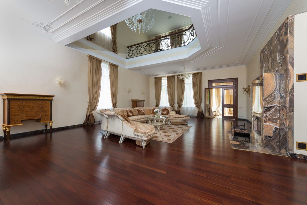 Modern Victorian living room with curved seating, dark wood floors, ornate ceiling details, draped windows, and a marble fireplace.