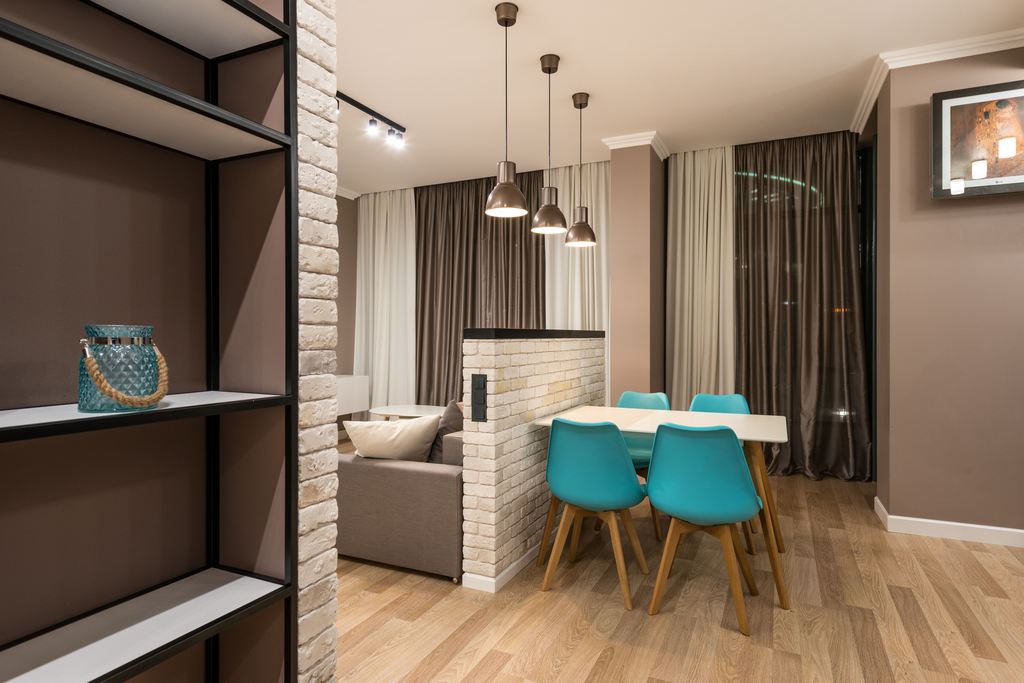 Rectangular dining table set beside a partial brick wall in a compact open-plan living space.