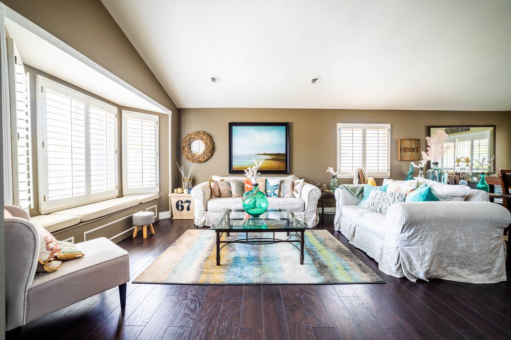 White sofas and armchair in a bright living room with dark wood floors and a colorful area rug