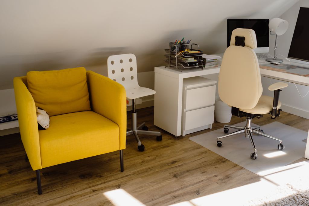 Home office corner with a white desk, dual monitors, rolling chair, and yellow armchair.