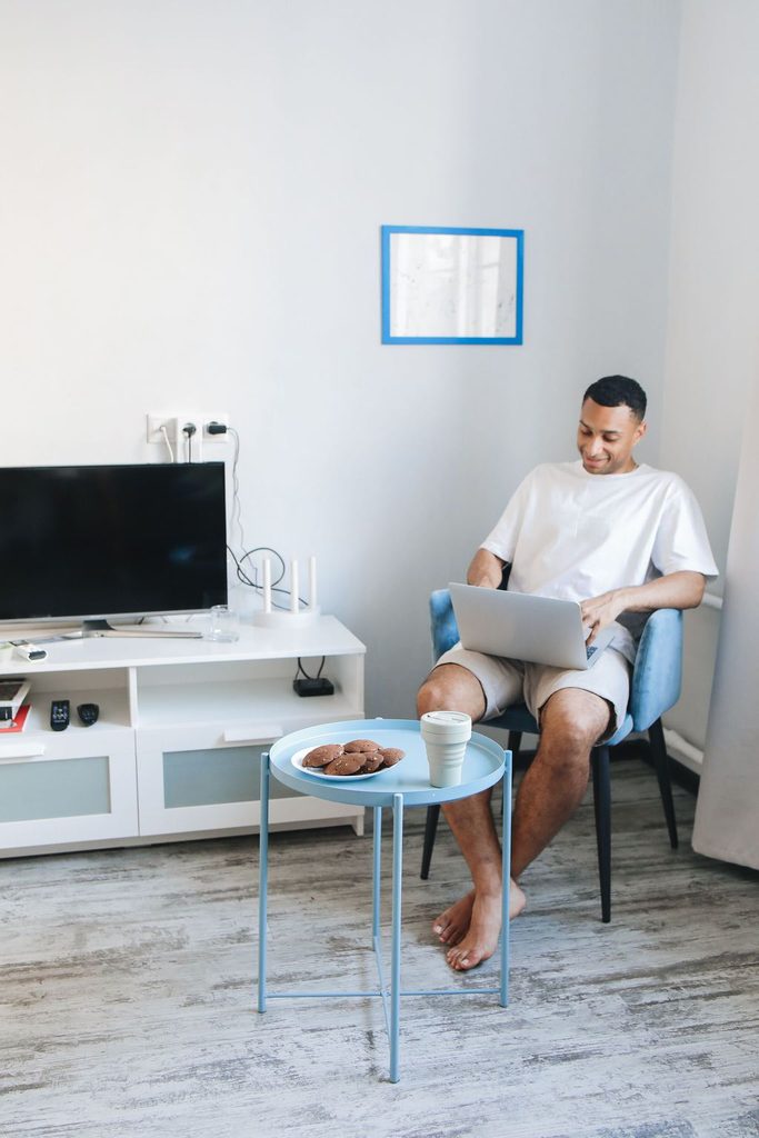Man using a laptop in a living room with a Wi-Fi router beside the TV on a media console.
