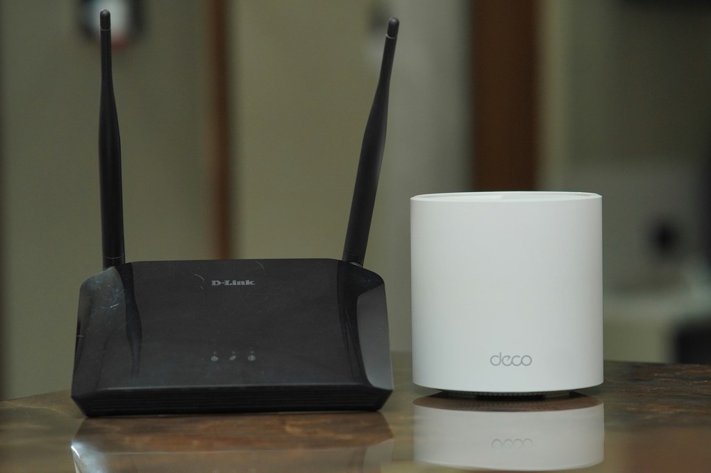 Black Wi-Fi router with antennas beside a white mesh Wi-Fi unit on a wooden table.