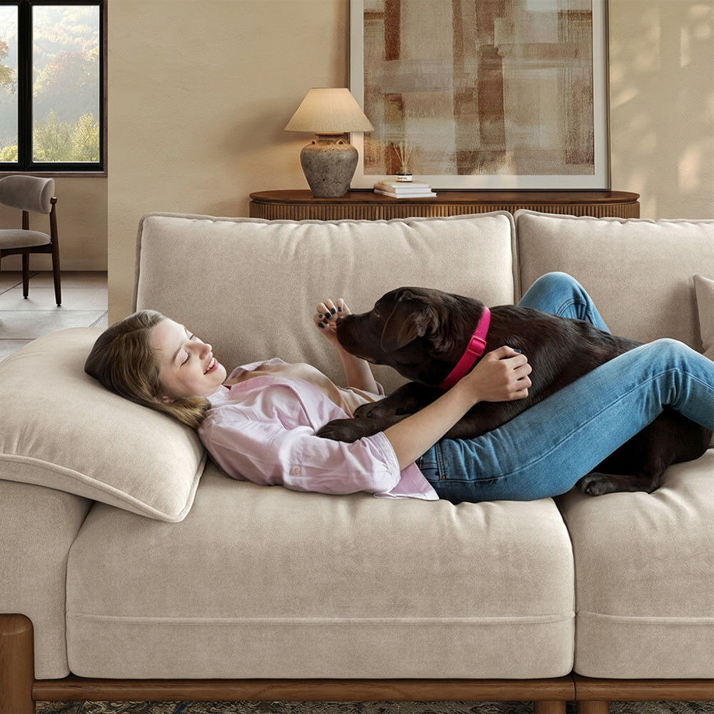 Woman relaxing on a beige sofa with a black dog in a warm, modern living room.