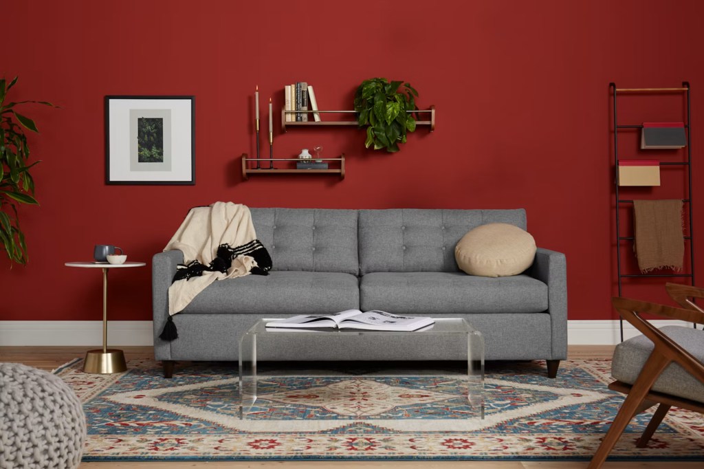Gray mid century modern sleeper sofa with tufted cushions in a living room with red walls.