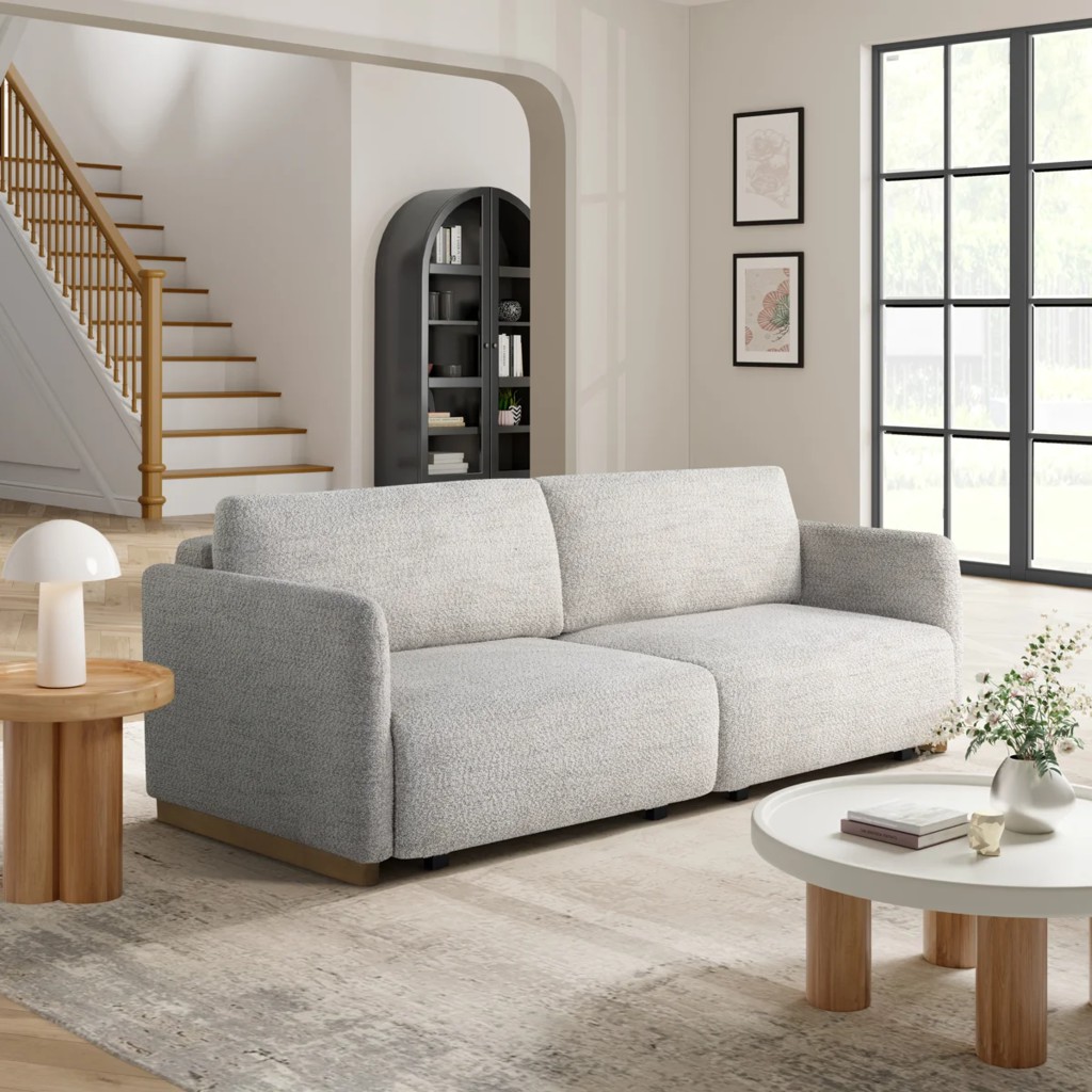 Light gray wall-hugger sleeper sofa in a bright modern living room with large windows and neutral decor.