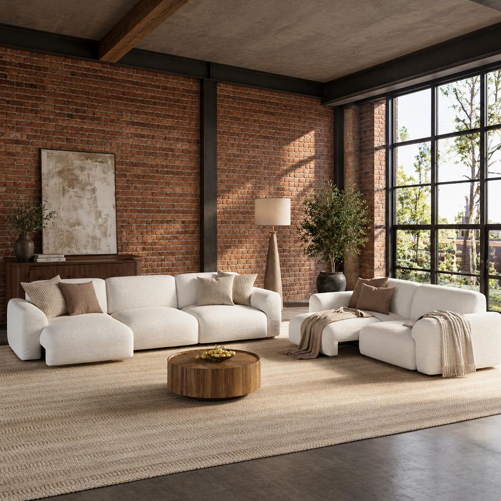 Industrial living room with exposed red brick walls, cream sofas, a walnut coffee table, black metal window frames, and a neutral woven rug.