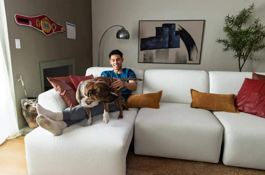 Man relaxing with his dog on a white modular sofa bed with extended seating in a bright living room.