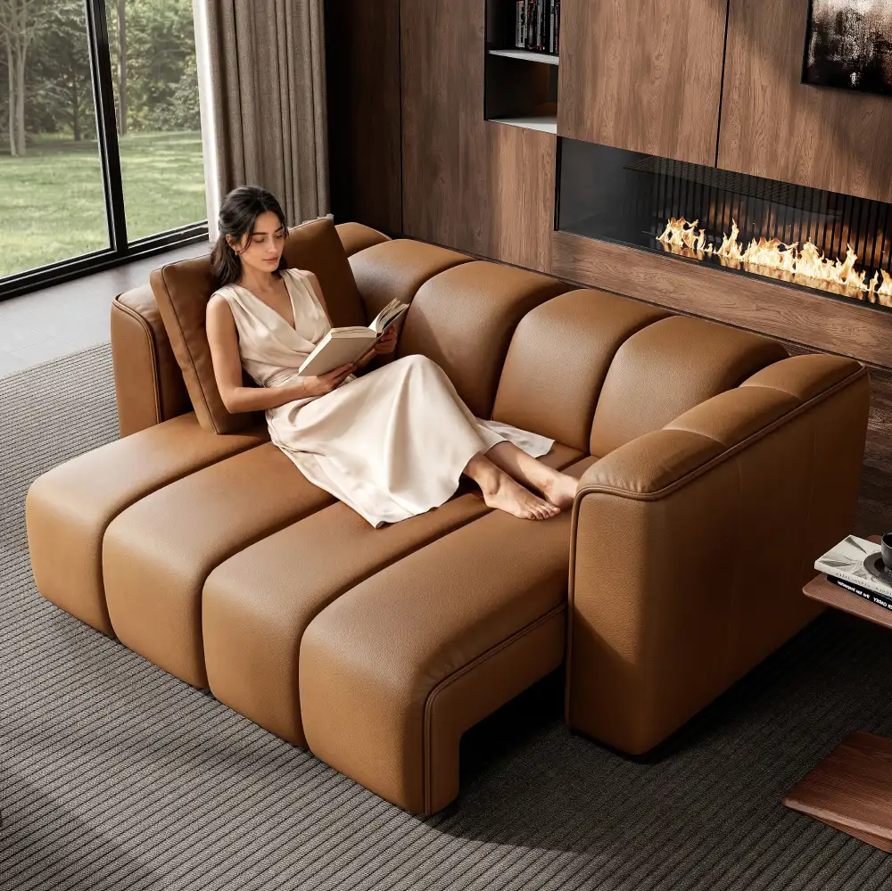 Woman reading on a brown leather power sofa bed with extended seats in a modern living room featuring a fireplace.