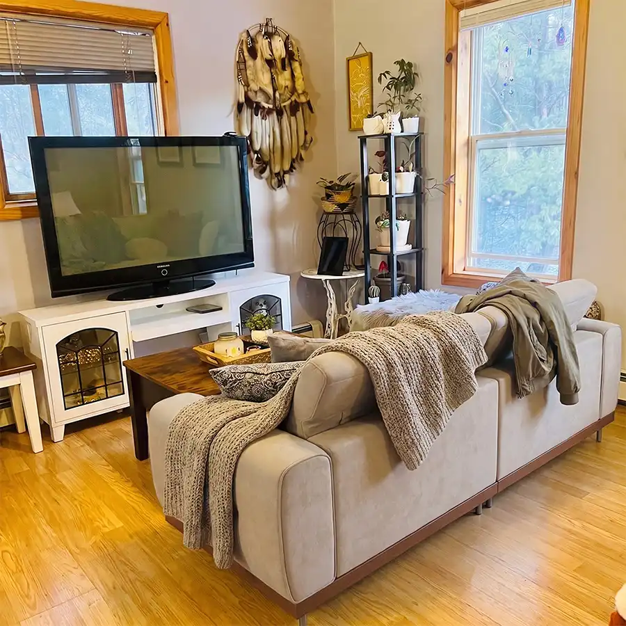 Compact beige sofa facing a TV in a cozy small living room, with a wooden coffee table, soft throws, and a clear walkway behind the seating.