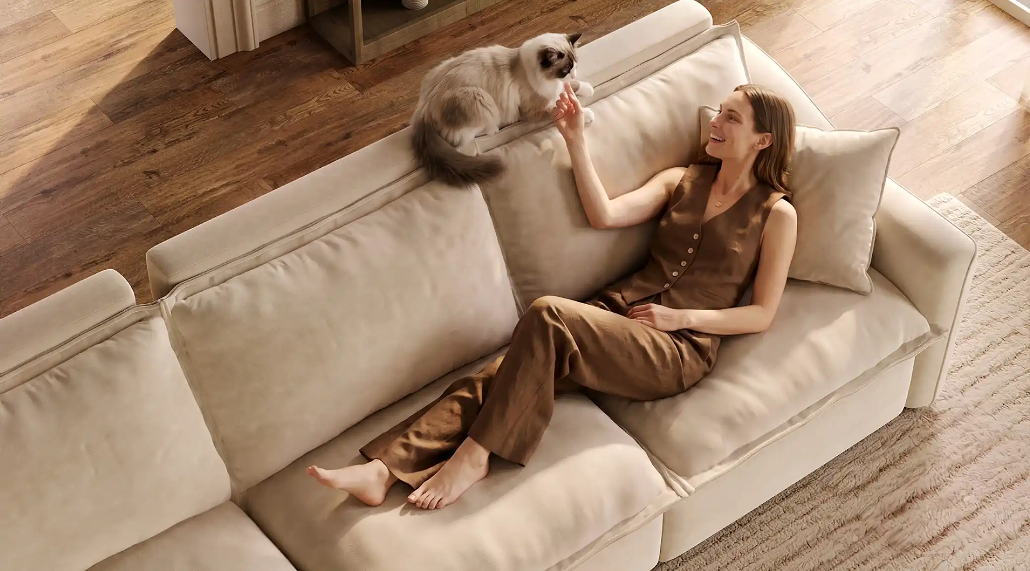 Woman relaxing on a cream-colored sofa with extended seating while interacting with her cat.