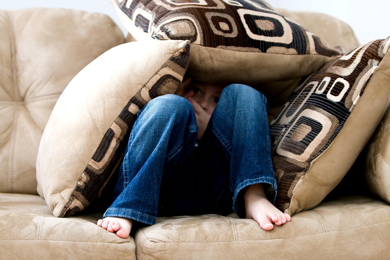 Little boy playing behind couch cushions in the living room