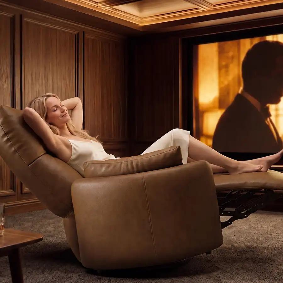 Woman relaxing in a brown leather recliner with the footrest extended in a home theater with a large movie screen.