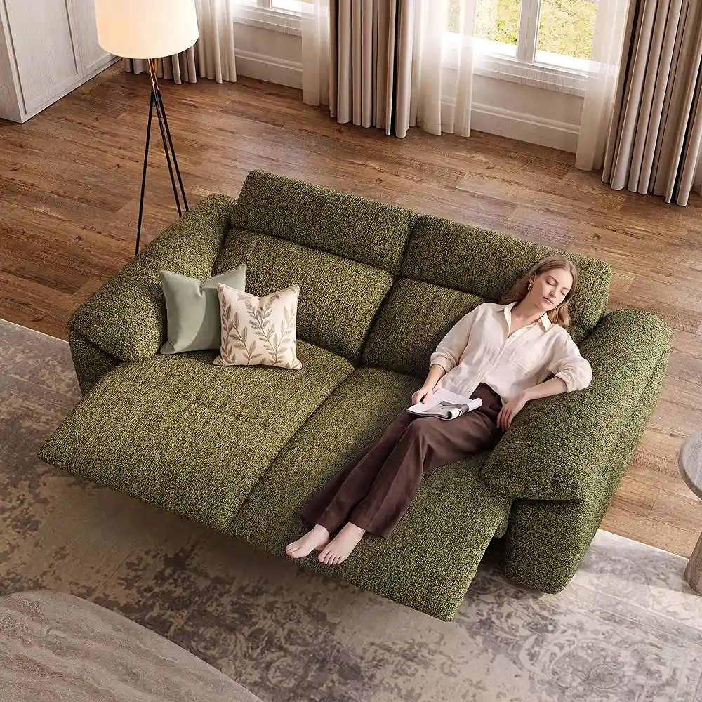 Green reclining sofa with an extended footrest and a woman relaxing with a book in a bright living room.