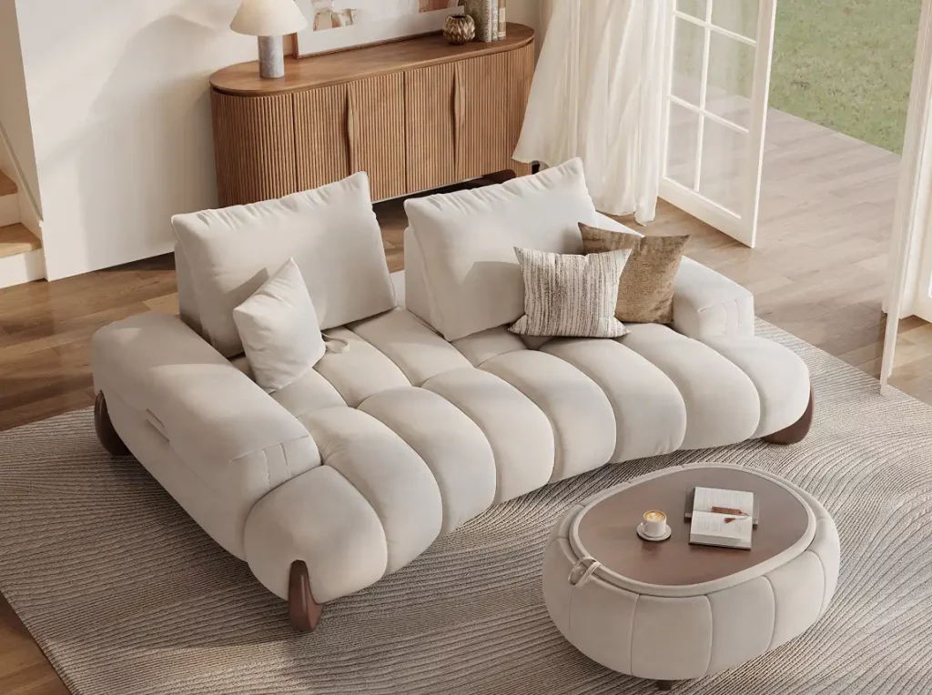 White deep-seat sofa with oversized back cushions, rounded arms, and matching accent pillows beside a round coffee table in a sunlit living room.