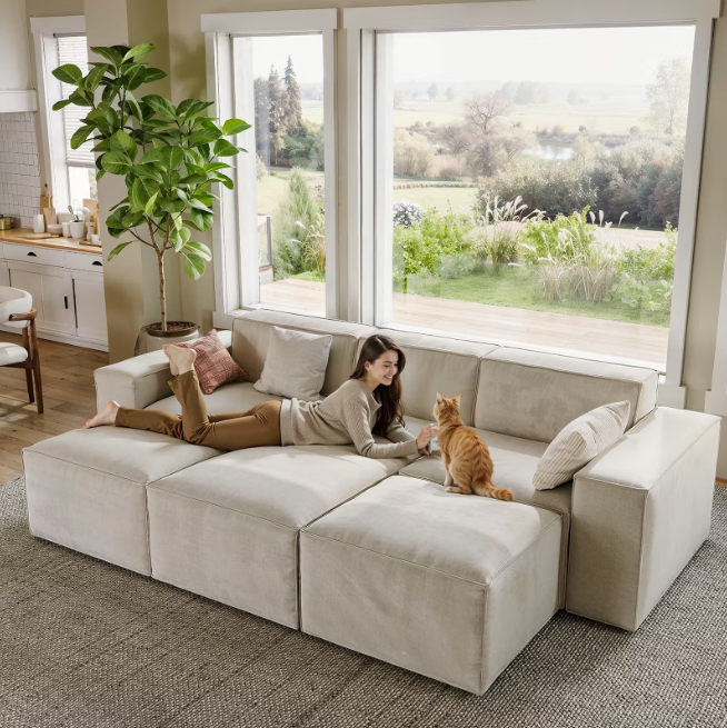 Woman relaxing with her cat on a beige modular sofa in a bright, spacious living room.
