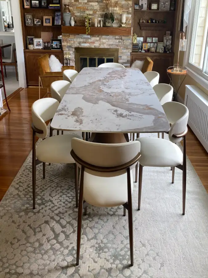 Rectangular dining table with a white and gray marble-look top, surrounded by cream upholstered chairs in a traditional dining room.