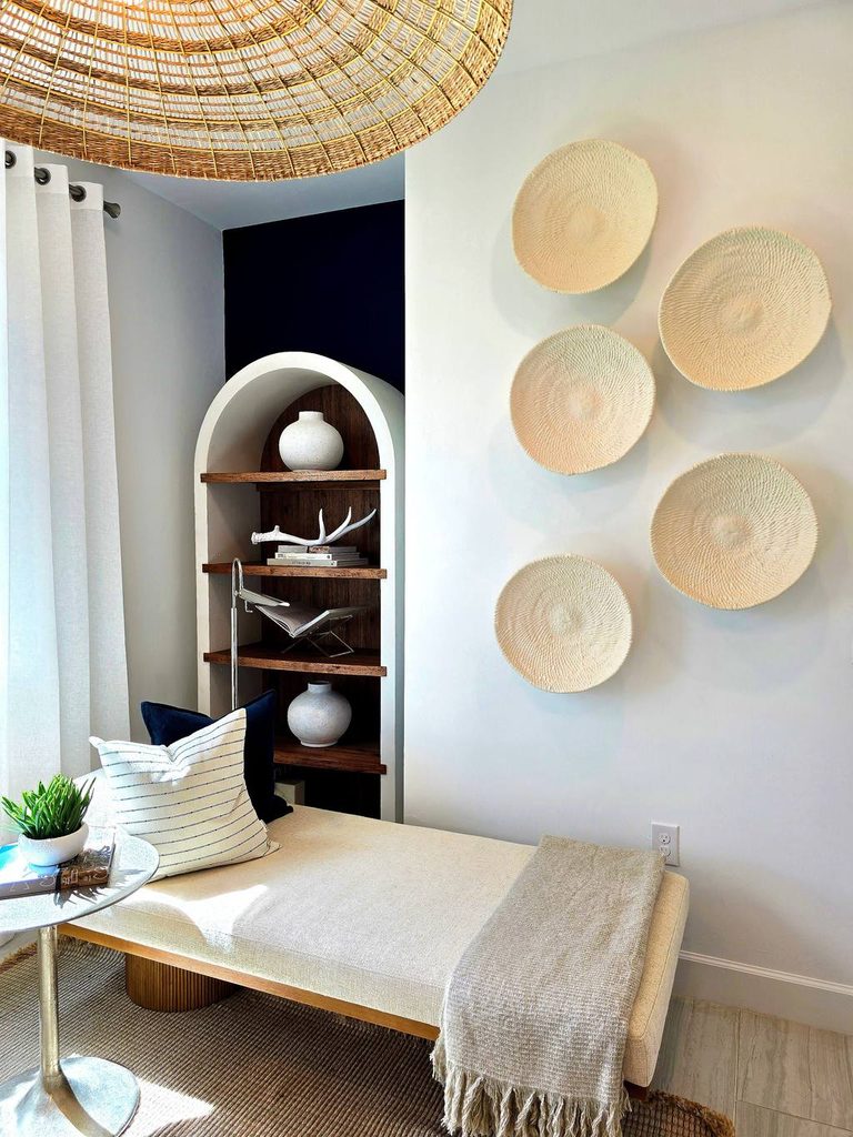 Upholstered daybed with a round side table, decorative wall baskets, and built-in shelving in a bright guest room.
