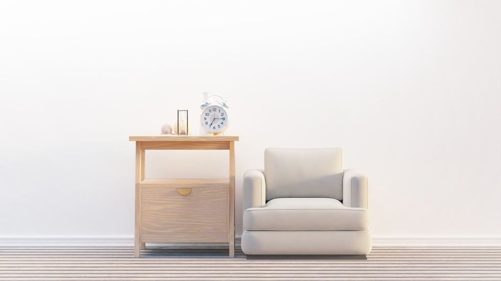 Minimalist living room corner with a white armchair beside a wooden side table against a bright white wall.