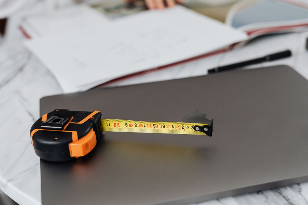 Tape measure stretched across a tabletop with design plans in the background, illustrating DIY sofa bed measurements and planning.