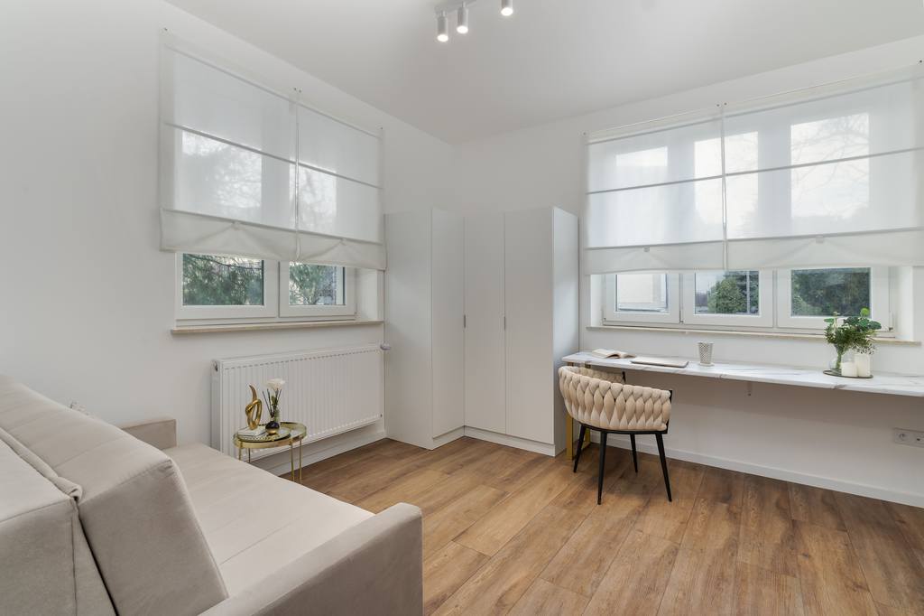 Small guest room with a sofa, built-in wardrobe, and wall-mounted craft desk beneath large windows.