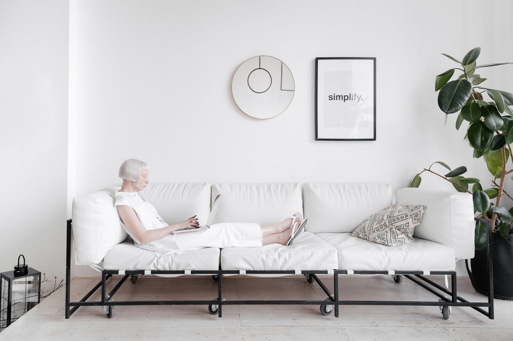Woman using a laptop while reclining on a white sofa with an extended metal frame, illustrating a DIY sofa bed design for lounging.