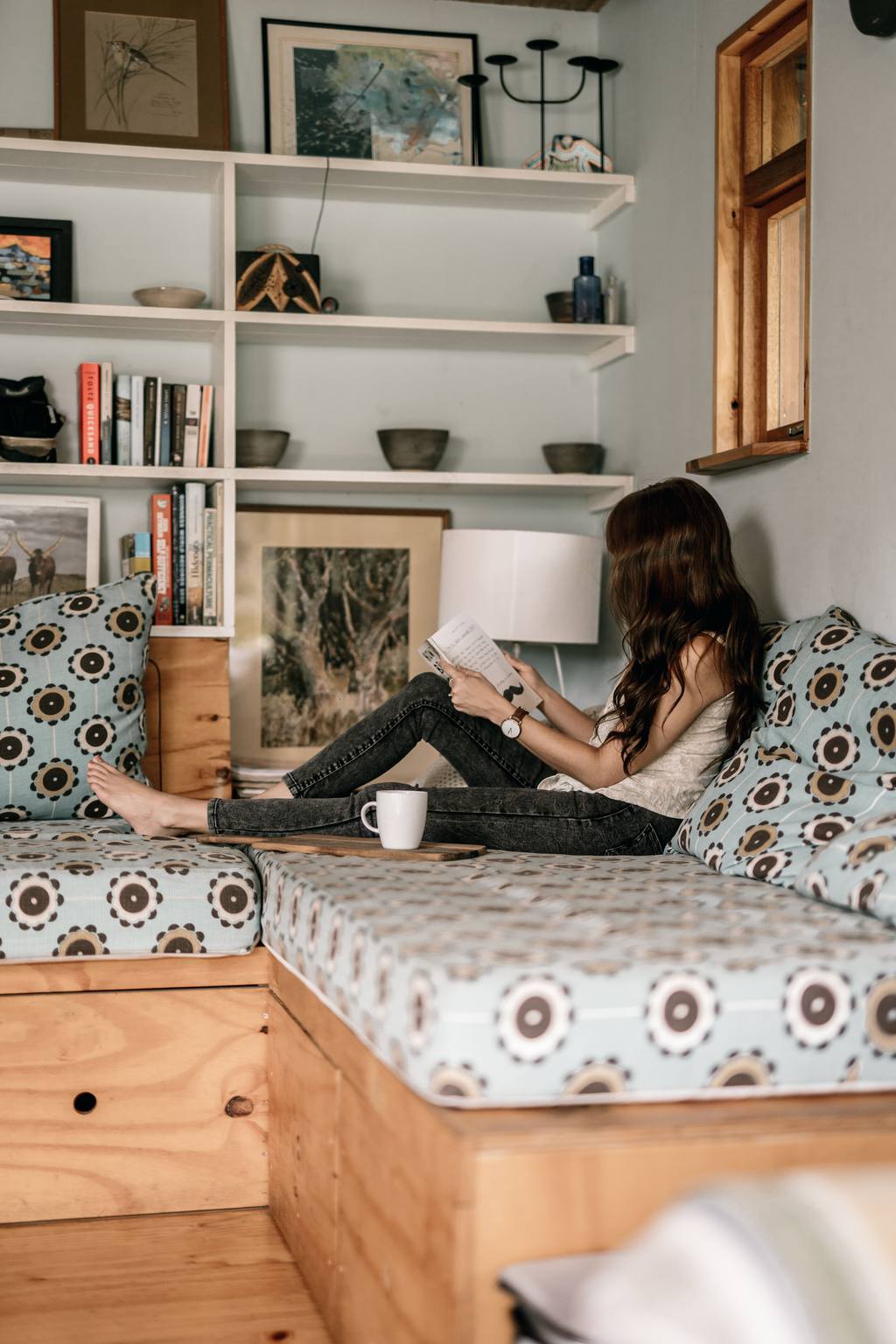 Woman relaxing with a book on a DIY wooden sofa bed with patterned cushions in a cozy living room.