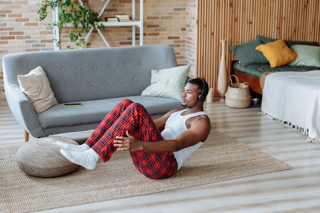 Man exercising on a rug in a multipurpose guest room with a gray sofa, bed, and open floor space.